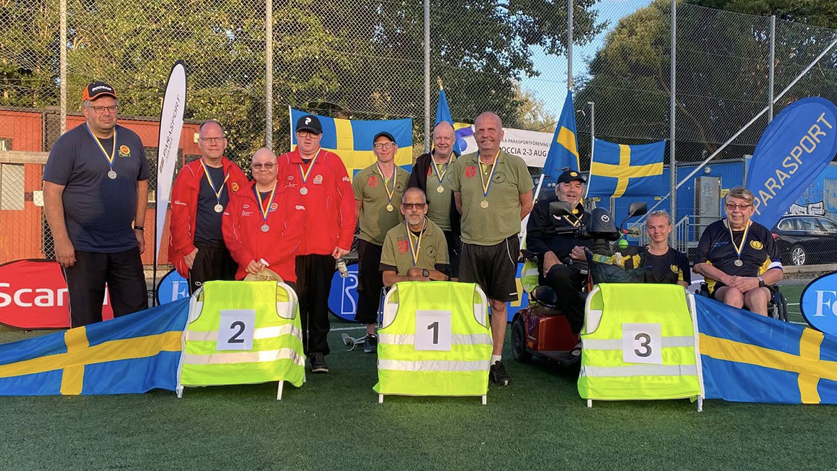De tre lag som tog medalj står uppradade på spelplanen. Svenska flaggor flankerar spelarna.
