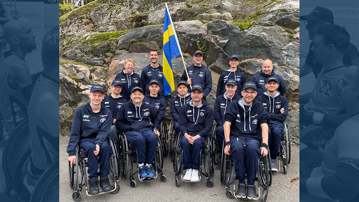 Gruppfoto på det svenska laget iklädda mörkblå träningskläder. I mitten hålls den svenska fanan.