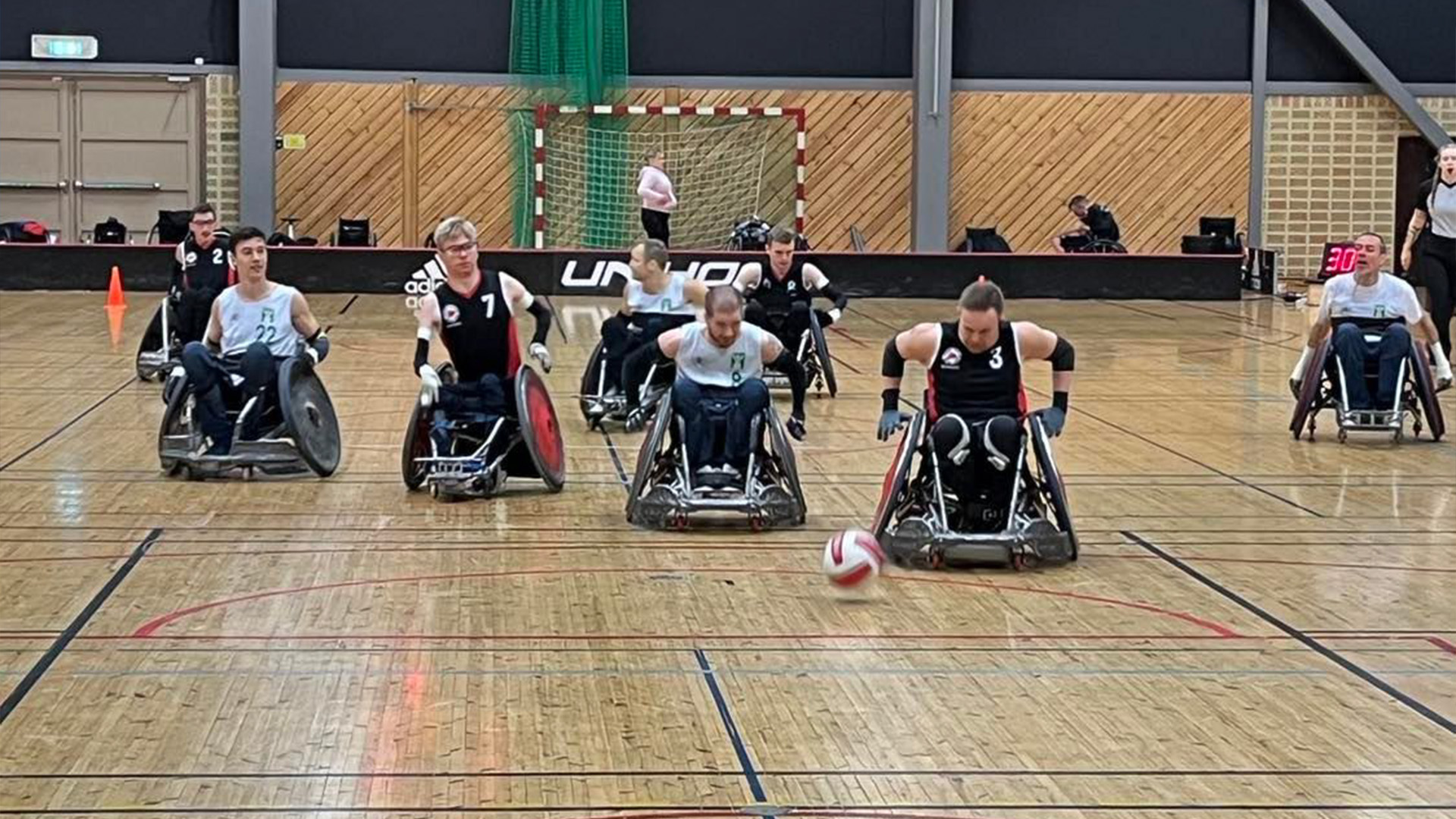 Bild på en match i rullstoslrugby. Flera spelare jagar efter en boll som rullar på golvet.