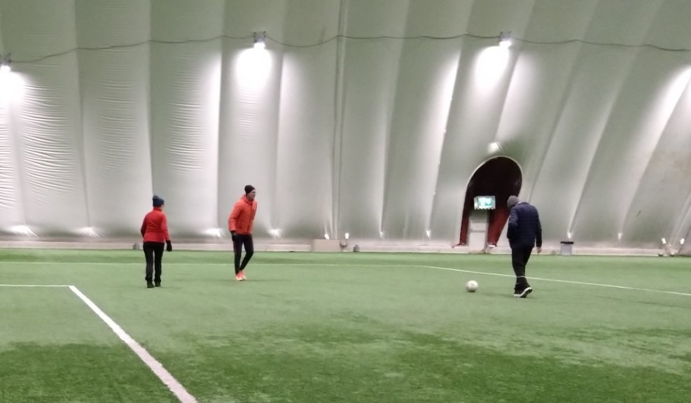 Tre spelare spelar gå fotboll  på planen i en idrottshall