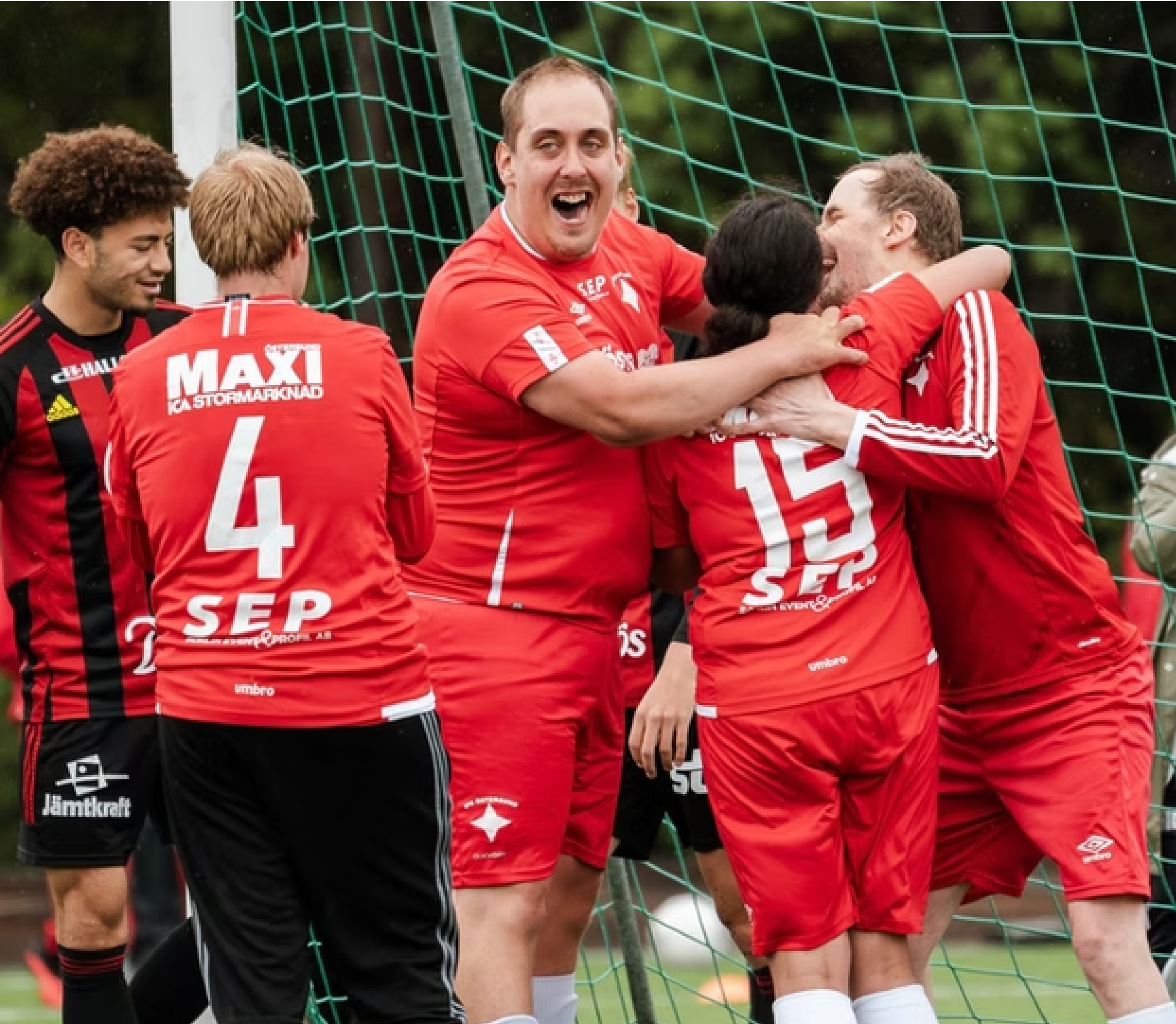 Glada fotbollsspelare i röda kläder, kramar om varandra vid ett mål.