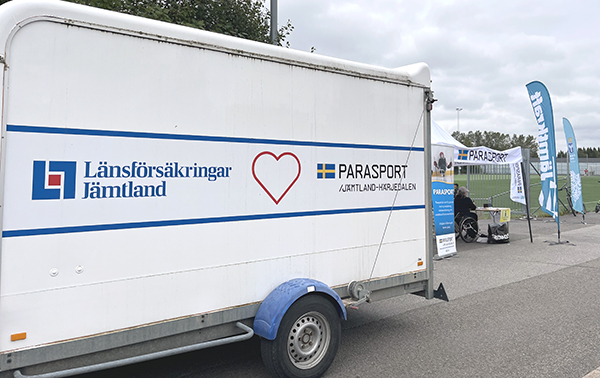 Parasportdagen 2025_Entrén. Släpvagn med vår och LF-logga. Lite längre bort, efter vårat Parasporttält, står beachflags Jämtkraft och Östersunds Kommun.