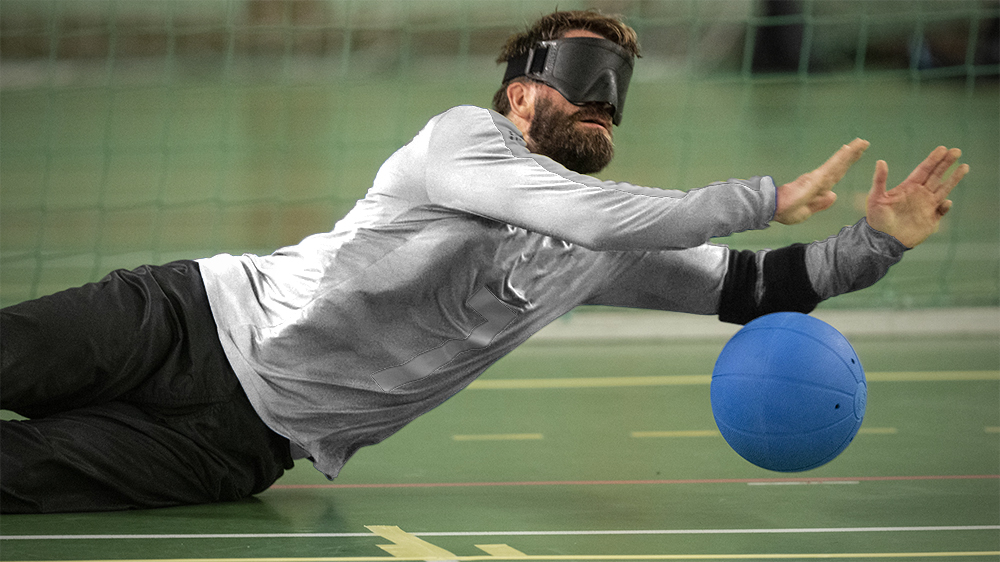 En spelare med ögonbindel slänger sig längs golvet och räddar bollen.
