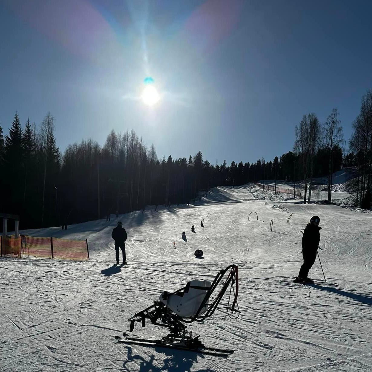 En biski i en slalombacke. Solen lyser och himmelen är blå. I backen syns två personer.