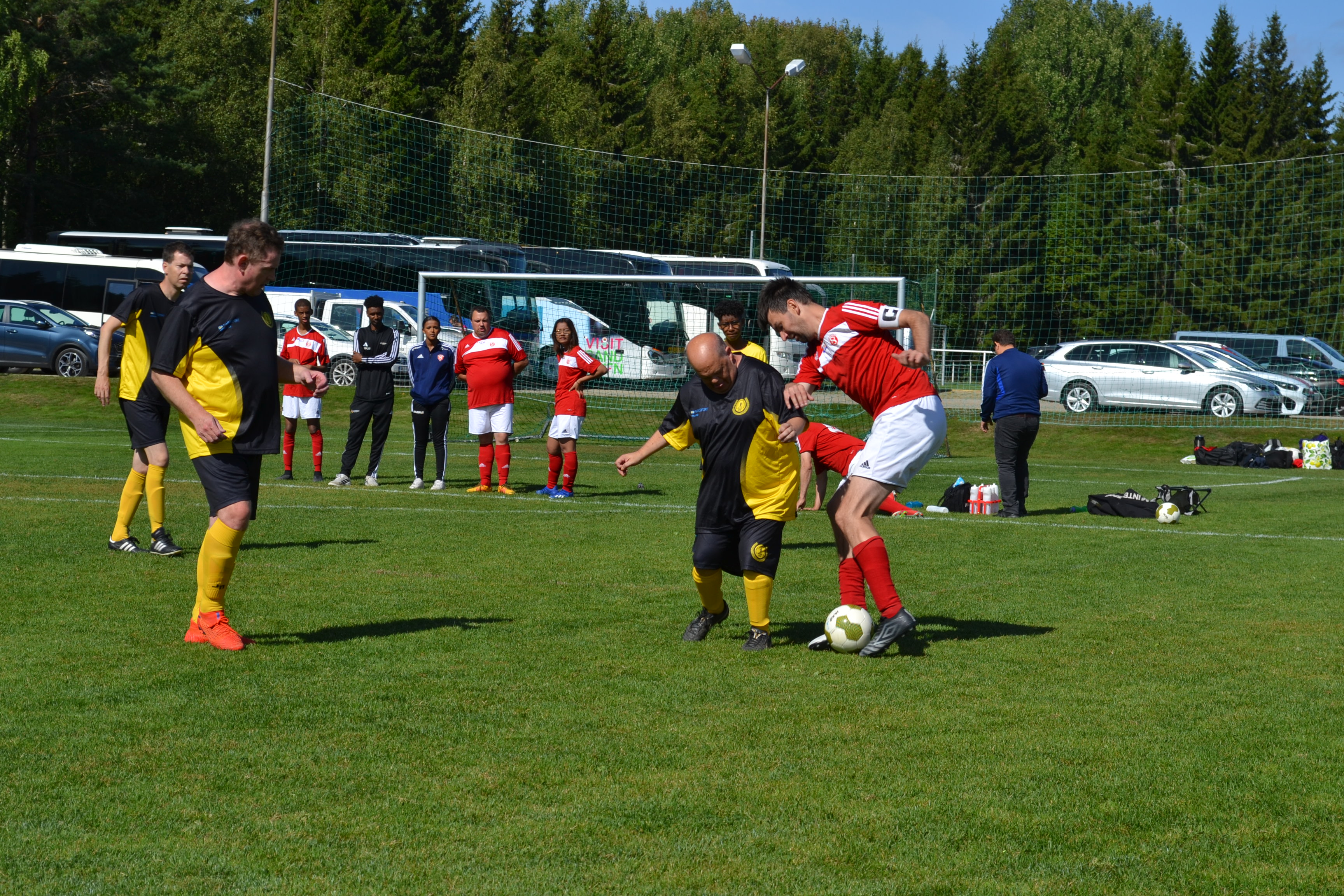 Fotbollsmatch under ett sammandrag i parafotboll där spelare från två lag kämpar om bollen på en gräsplan. I bakgrunden syns ledare, spelare och publik vid sidan av planen.