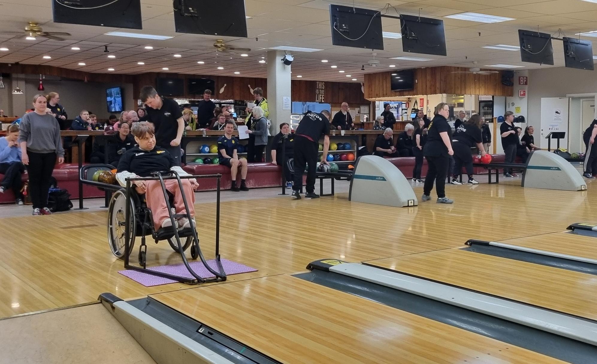 Deltagare i Hälsingestriken samlade i Bollnäs Bowlinghall, där både stående och sittande spelare deltar i en inkluderande tävlingsmiljö med publik och lagkamrater i bakgrunden.