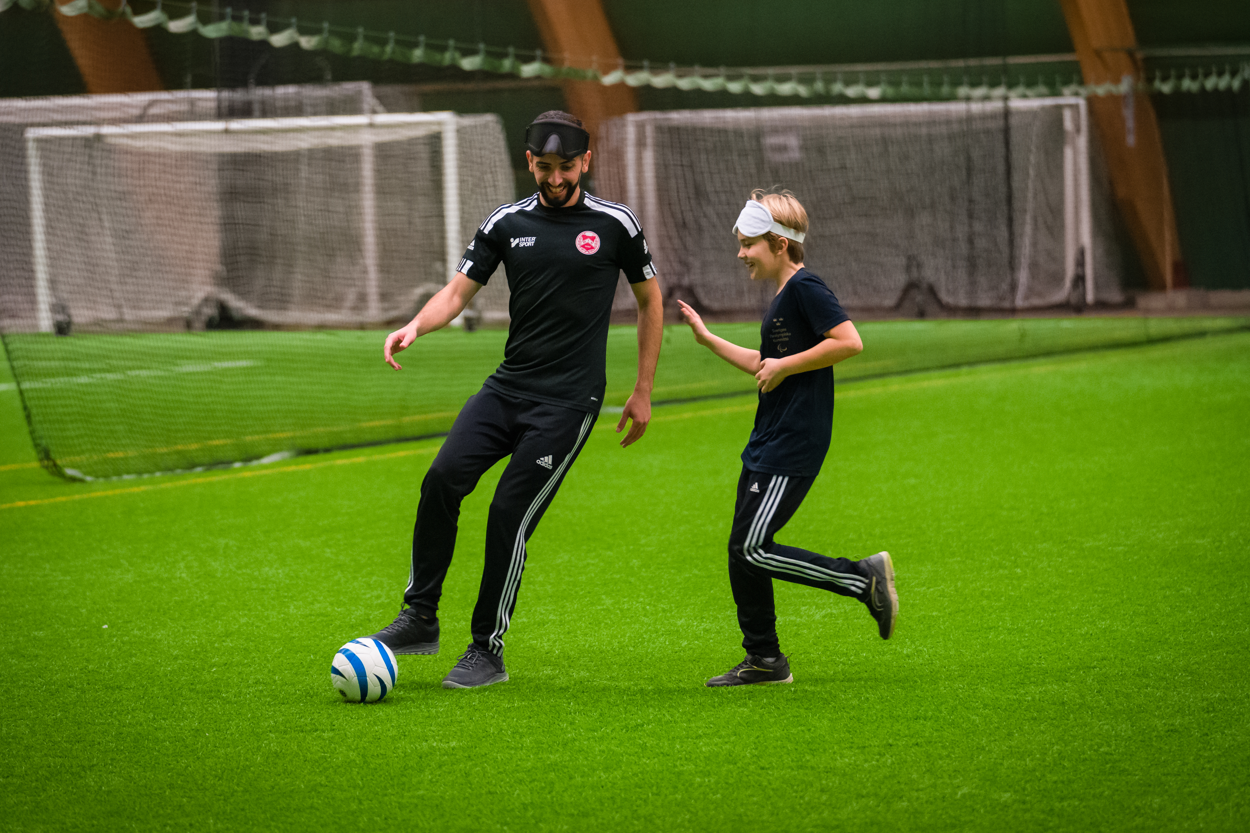 Foto, fotbollsplan inomhus. Abdullah dribblar fotbollen tillsammans med en ung kille.
