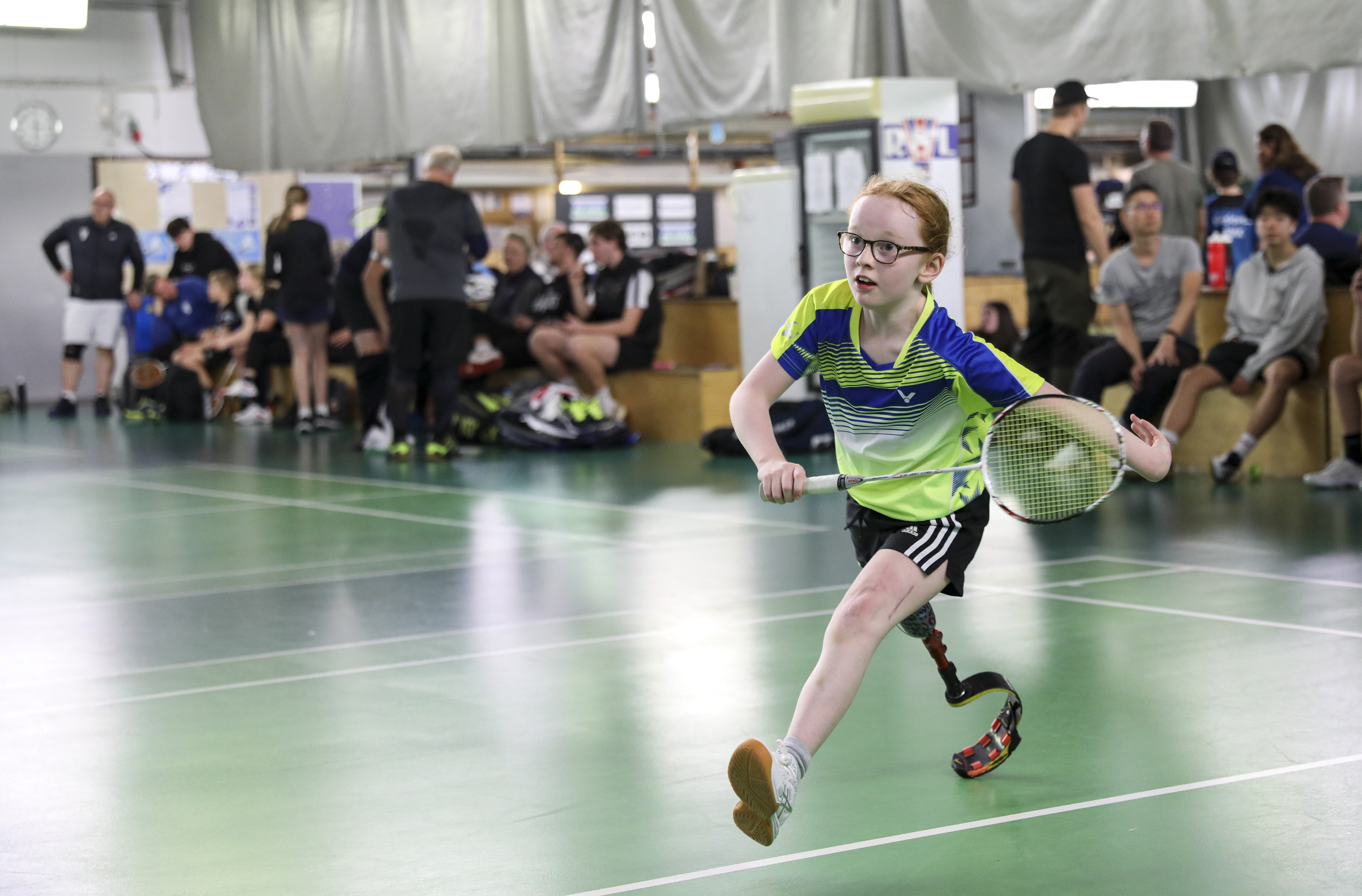 Foto, badmintonhall inomhus. En ung flicka mitt i steget att få en träff på badmintonbollen.