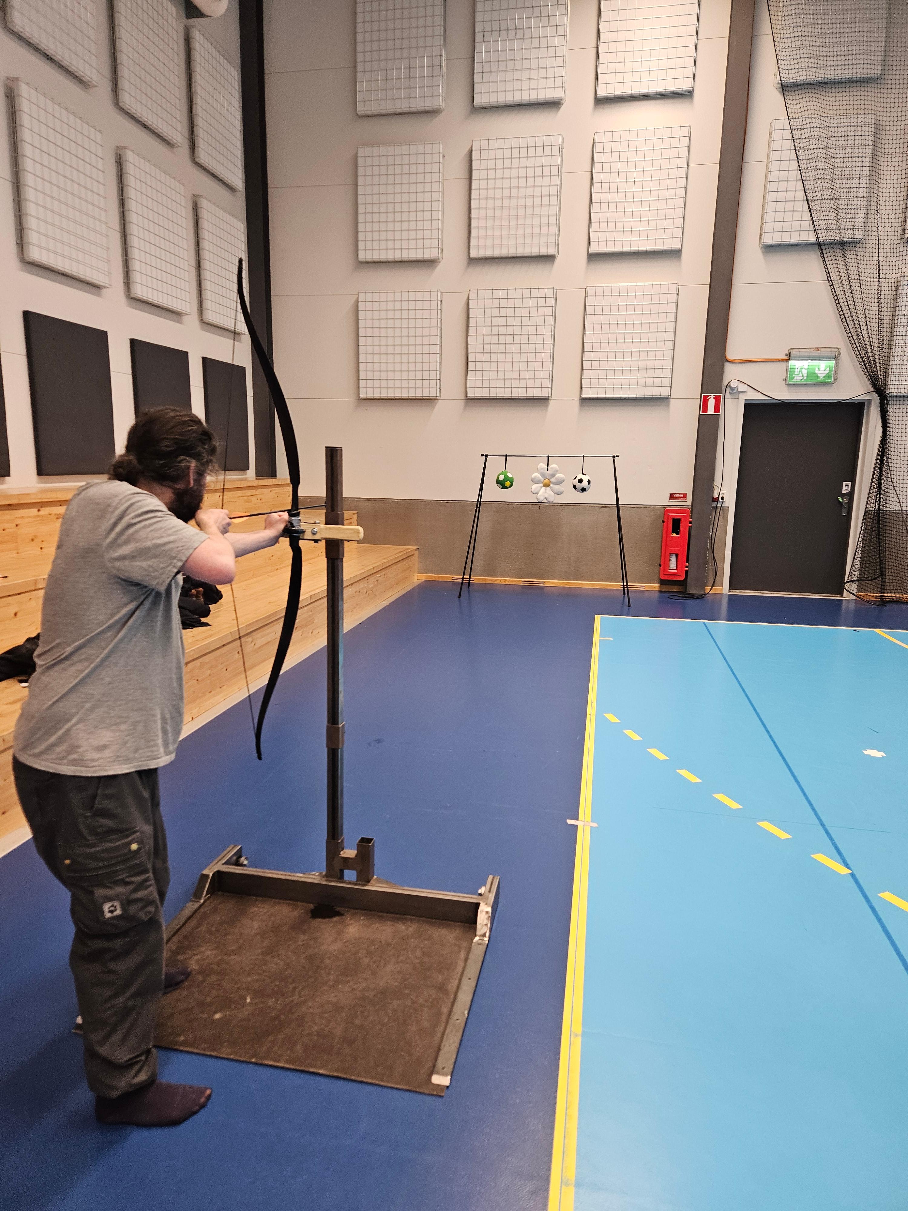 En person provar på bågskytte och står och stiktar. Bågen sitter fast i en ställning för att öka tillgängligheten till bågskytte.