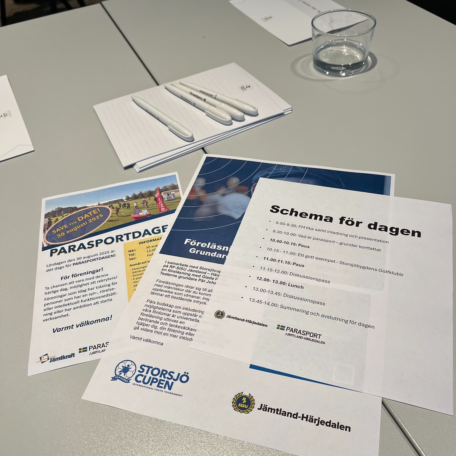 Lite papper på ett bord. Bl.a. Schema för dagen, föreläsning med Pär Johnsson och Save the Date inför Parasportdagen