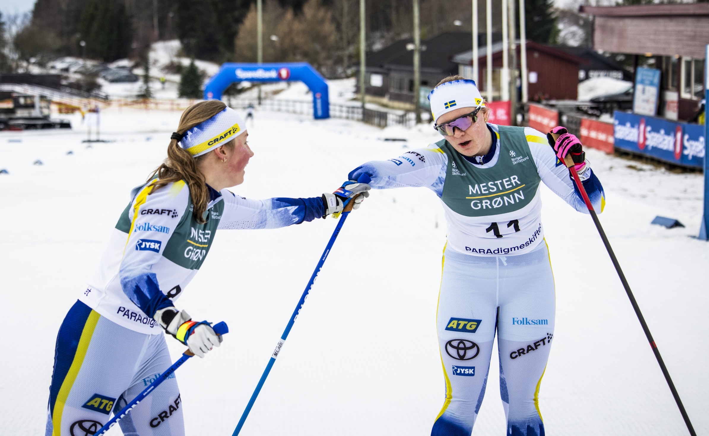 Foto, utomhusmiljö. Två kvinnliga längdskidåkare i svenska landslagskläder gratulerar varandra efter upploppet.
