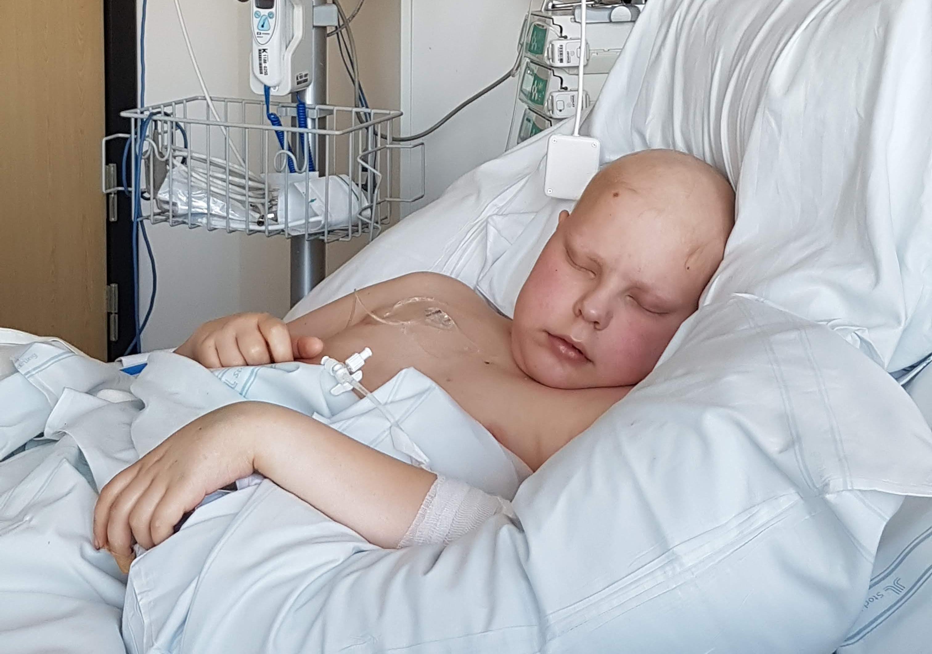 Foto, inomhus. Oscar som 12-åring, sovandes i en sjukhussäng omgiven av apparater. 