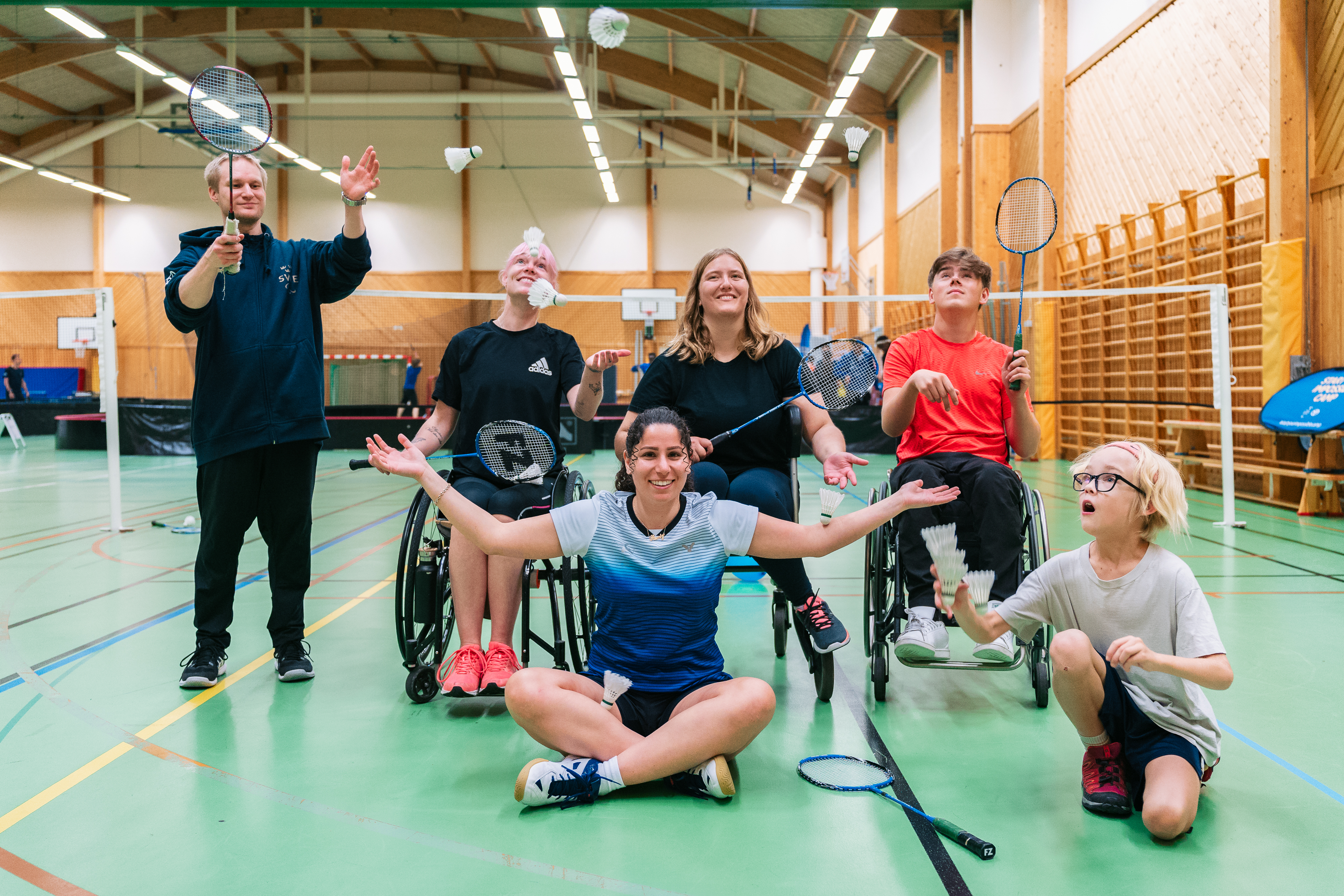 En grupp parasportare med sin tränare på en badmintonplan. 
