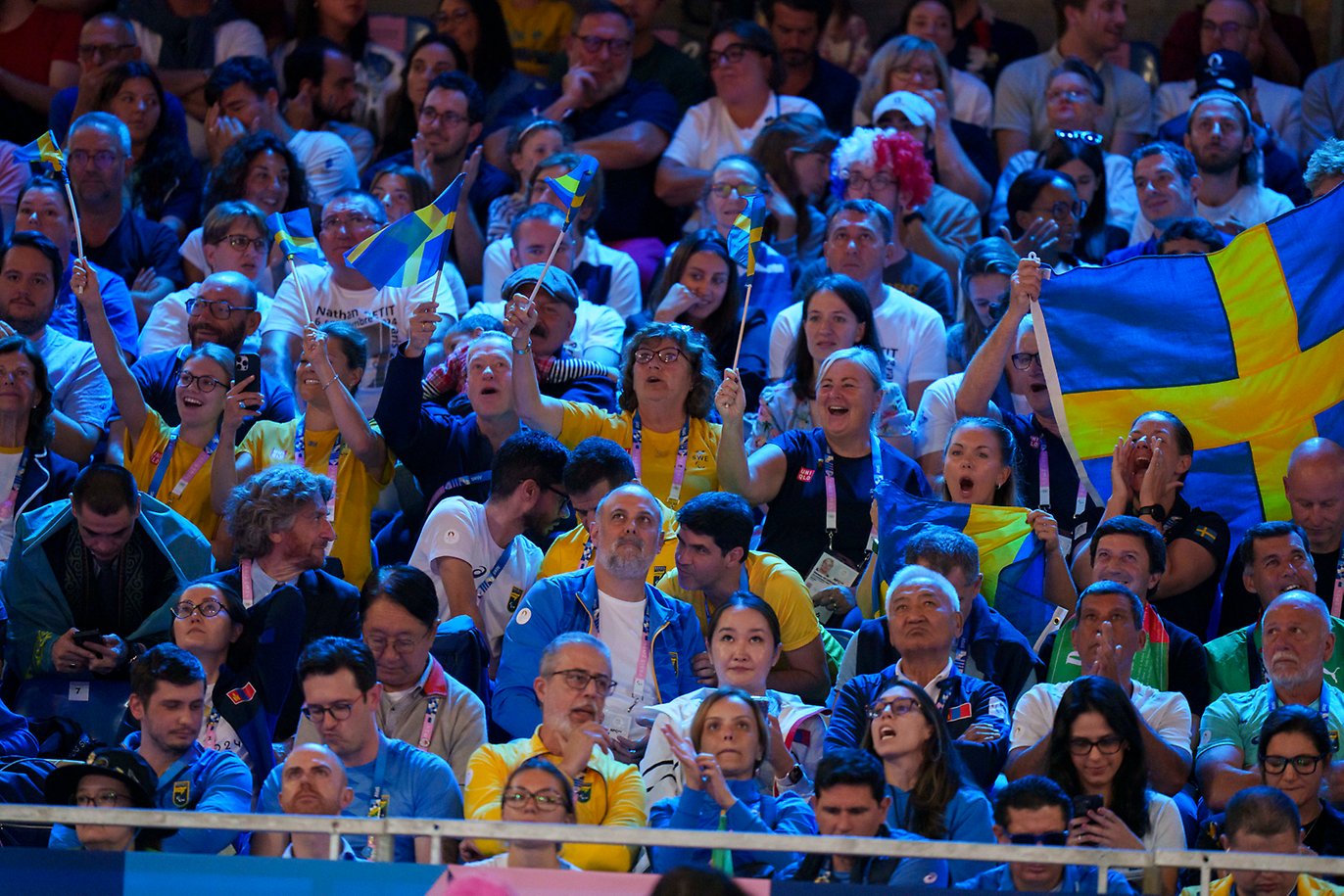 De svenska fansen jublar och viftar med svenska flaggor på läktaren under Paralympics i Paris.